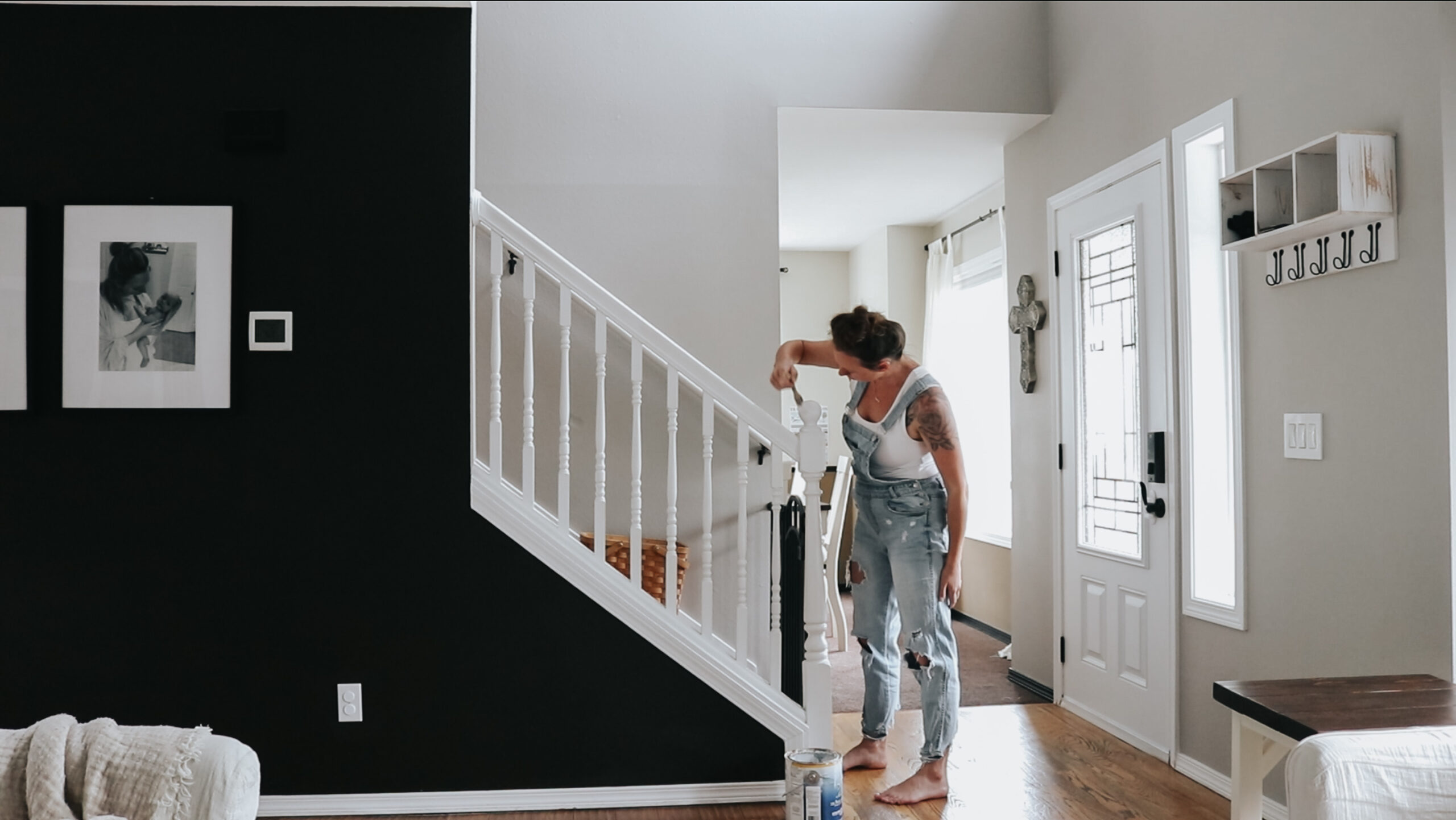 Christian homemaker wearing a white tank top and jean overalls is painting the stairwell banister white